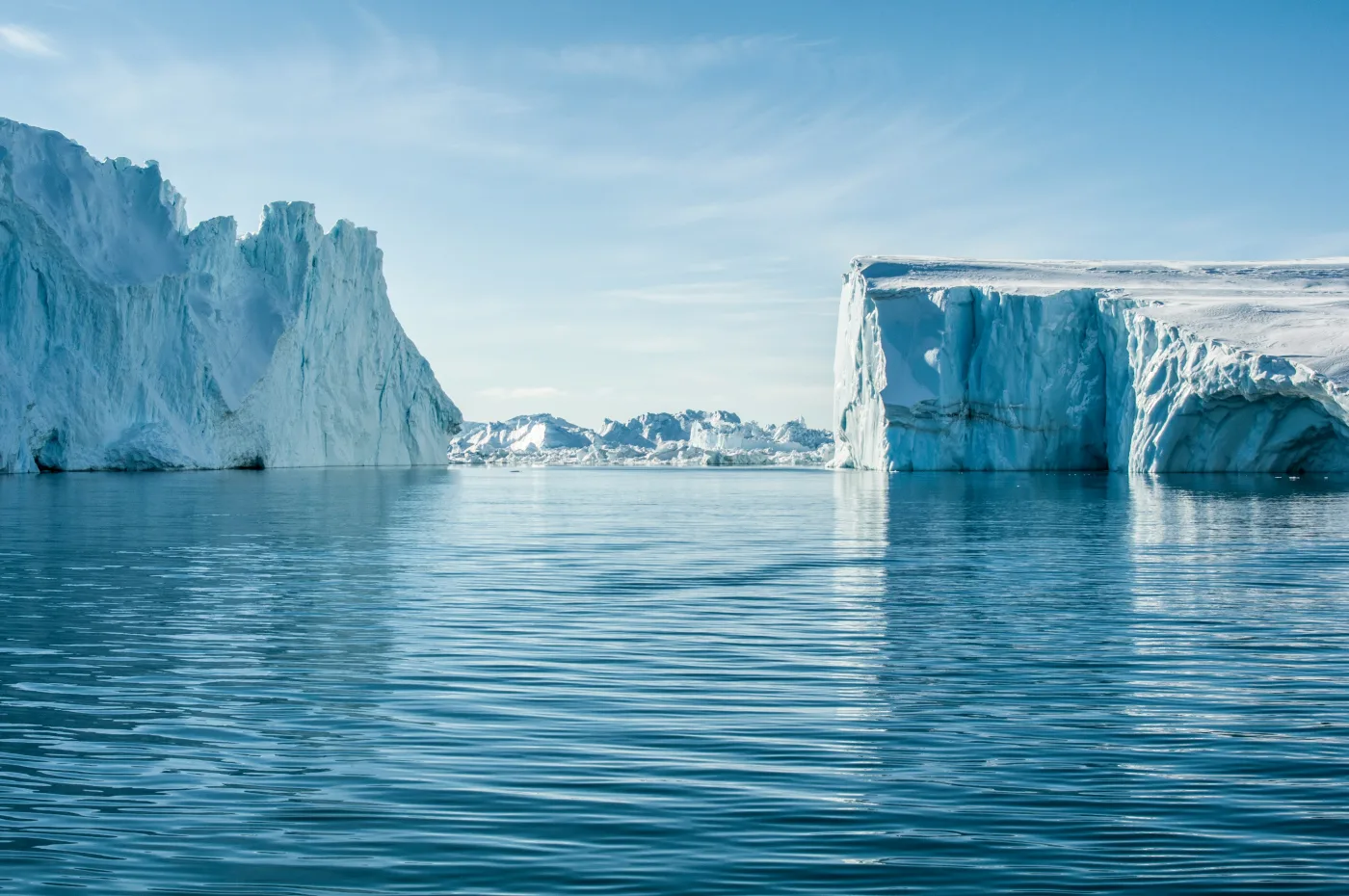 Towering icebergs drift through the waters off northwestern Greenland, not far from the Prudhoe Dome drill site. New luminescence dating from sediments beneath 509 metres of ice confirms this entire region was ice-free just 7,100 years ago — during a period of Arctic warmth that resembles what climate models project for the end of this century. Photo: Tina Rolf / Unsplash.