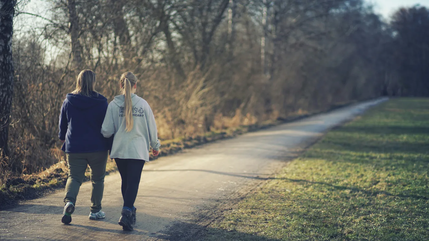 Two people take a leisure walk along a sunlit park trail — exactly the kind of low-intensity daily movement that a 2025 NIH and University of Oxford study found can reduce cancer risk by up to 26%. Research now shows that regular walking, even at a relaxed pace, carries meaningful protective health benefits. Photo by Unsplash.
