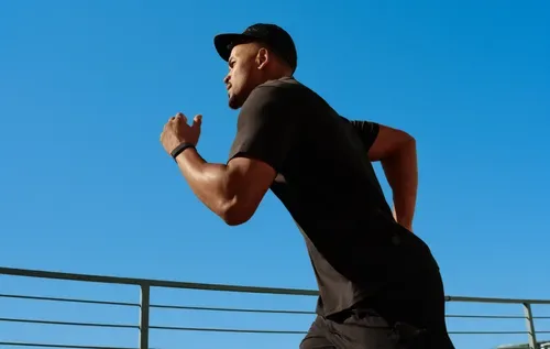 A runner in full sprint wearing the Fitbit Air on his left wrist, its slim screenless profile barely visible against the forearm — exactly how it's designed to be worn. The device auto-detects workouts like this in real time, logging pace, heart rate, and exertion without a single tap. Image: NavsoraTimes / Fitbit Air Feature, 2026.
