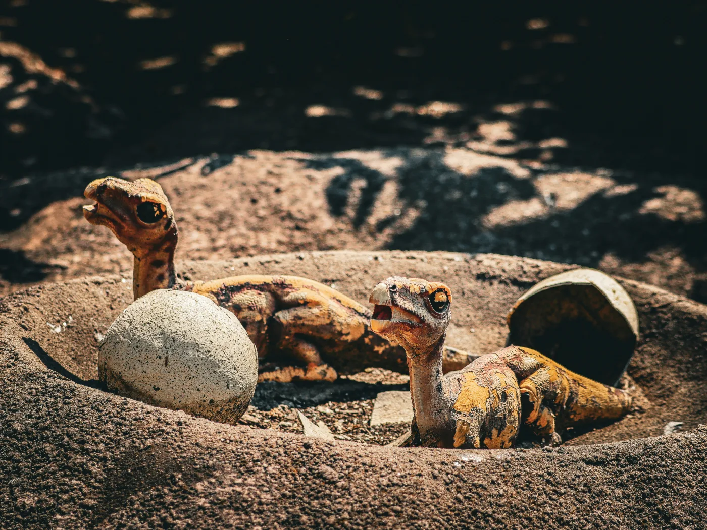 Two duck-billed dinosaur hatchlings climb out of a sandy nest with one unhatched egg and a cracked shell beside them, mouths open as if calling for food. Fossils from Maiasaura nesting sites in Montana suggest scenes like this one really did play out 75 million years ago, with parents arriving soon after to feed their young. Image credit: museum exhibit photograph.