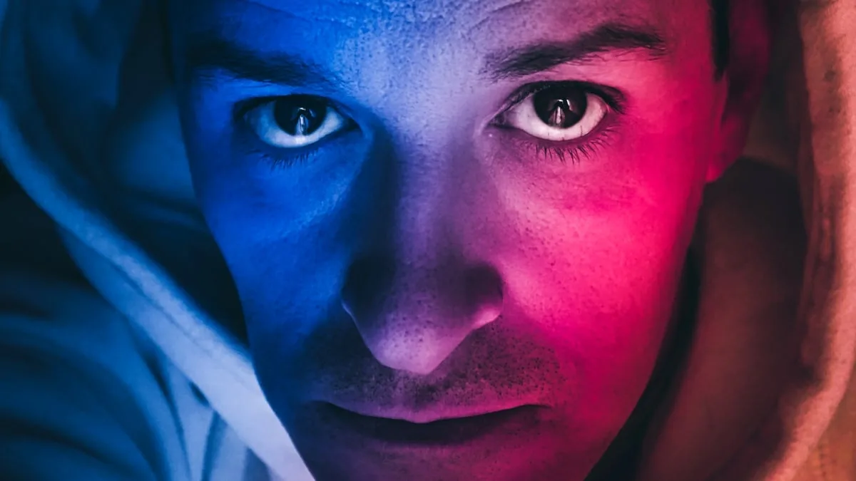 A man photographed in dramatic blue and red light, representing the invisible cellular changes that scientists now know are quietly reshaping the health of aging men. As some men grow older, certain cells in their body shed the Y chromosome entirely. Image: Cavan Images / Getty Images.